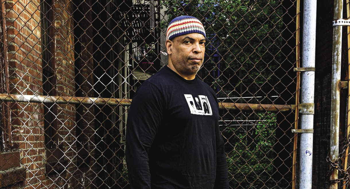 DJ Joaquin Joe Claussell posing in front of a chain link fence.