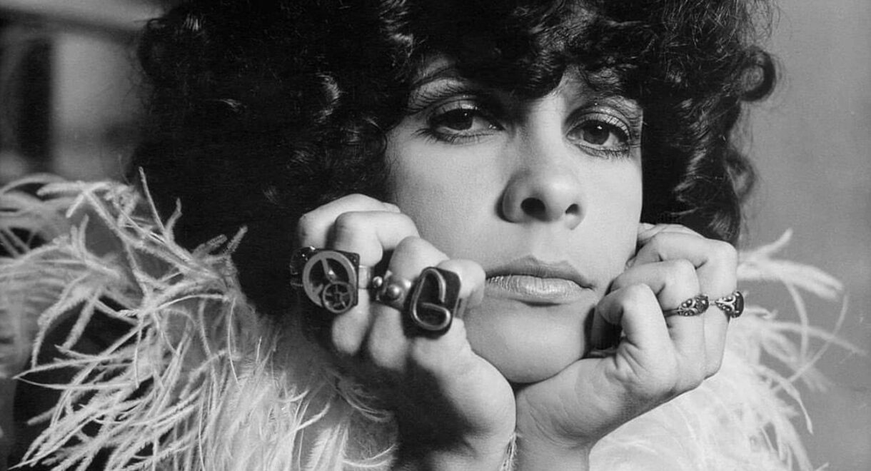 Gal Costa in the 1970s. She’s wearing a feather boa, big rings on her fingers and curly black hair.